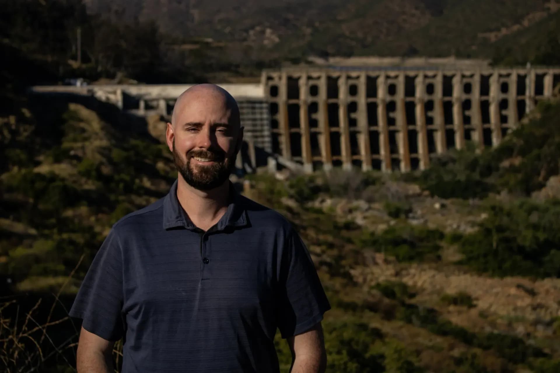 Jordan Keeney standing in front of a multiple-arch dam